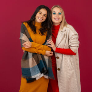 two smiling attractive stylish women in autumn winter fashion dress and coat posing isolated on red studio background