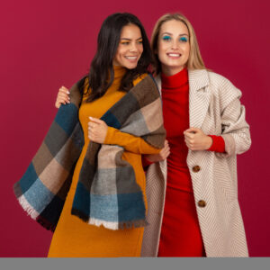 two smiling attractive stylish women in autumn winter fashion dress and coat posing isolated on red studio background